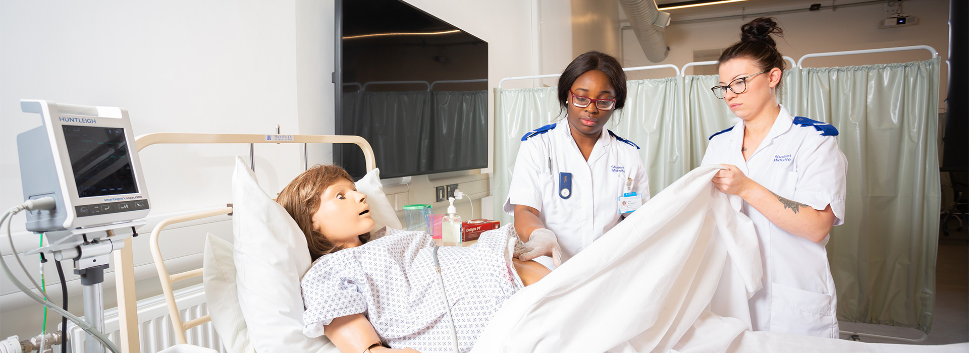 Two student midwives practicing on SimDoll.