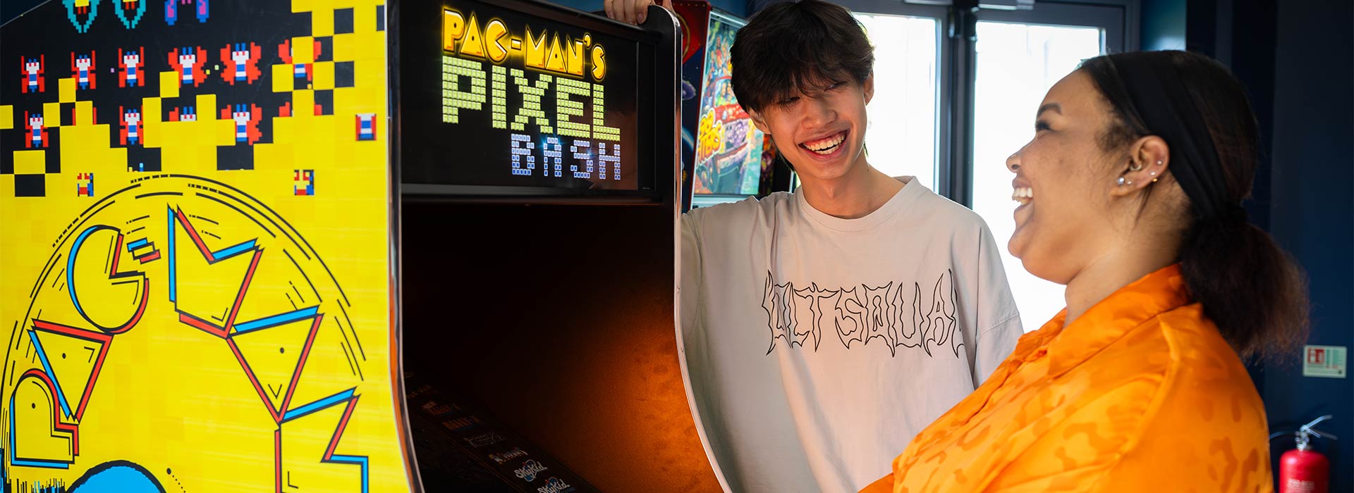 Two students playing on a retro Pac-Man games console.