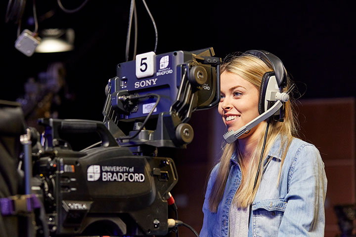Student in TV studio using video camera.