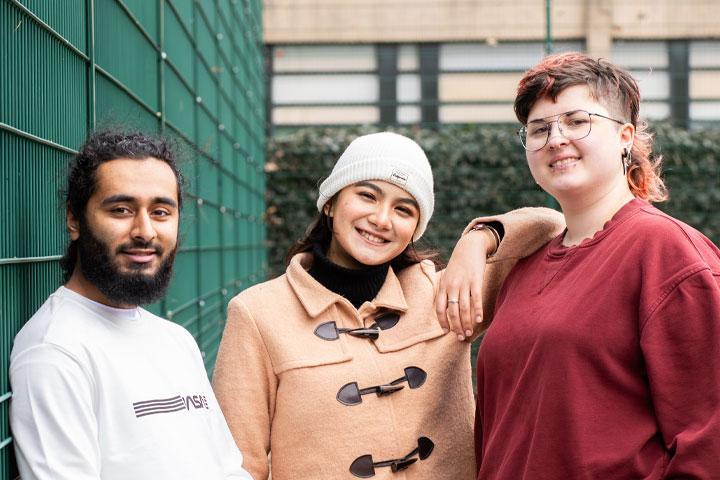 A group of three students standing together and smiling at the camera.