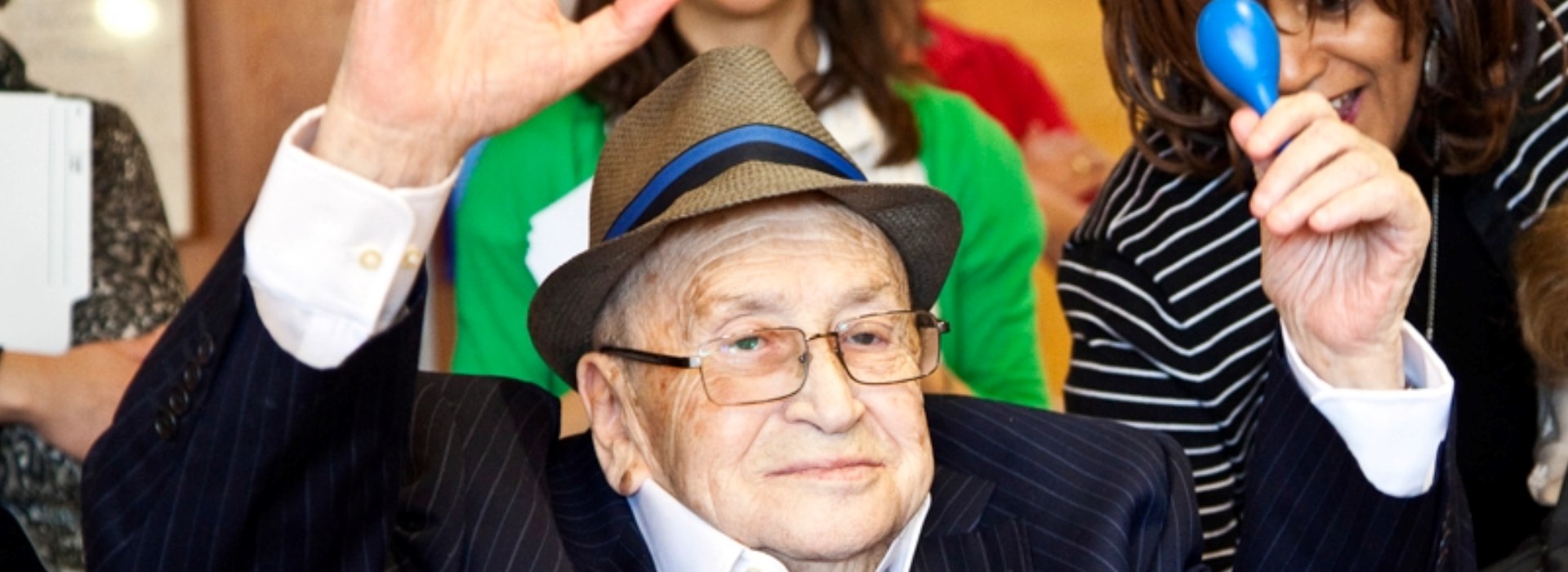 An image of an elderly man celebrating and holding a balloon with people smiling around him