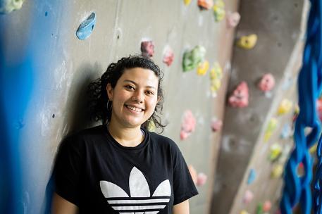 Student in front of on campus climbing wall smiling